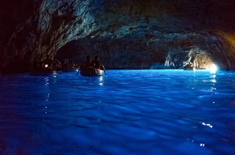 Люди катаются на лодках через водную пещеру, освещенную солнечным светом