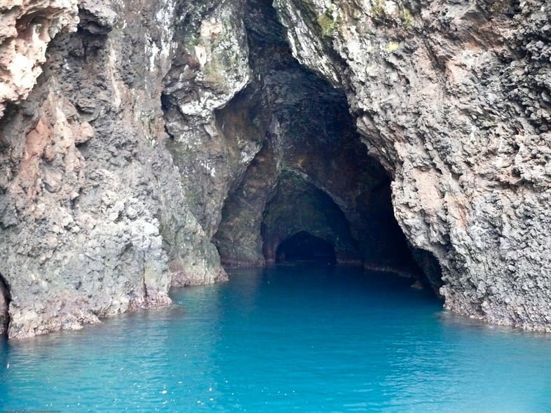 Вход в пещеру с ухабистыми каменными стенами и полом, покрытым ярко-голубой водой.