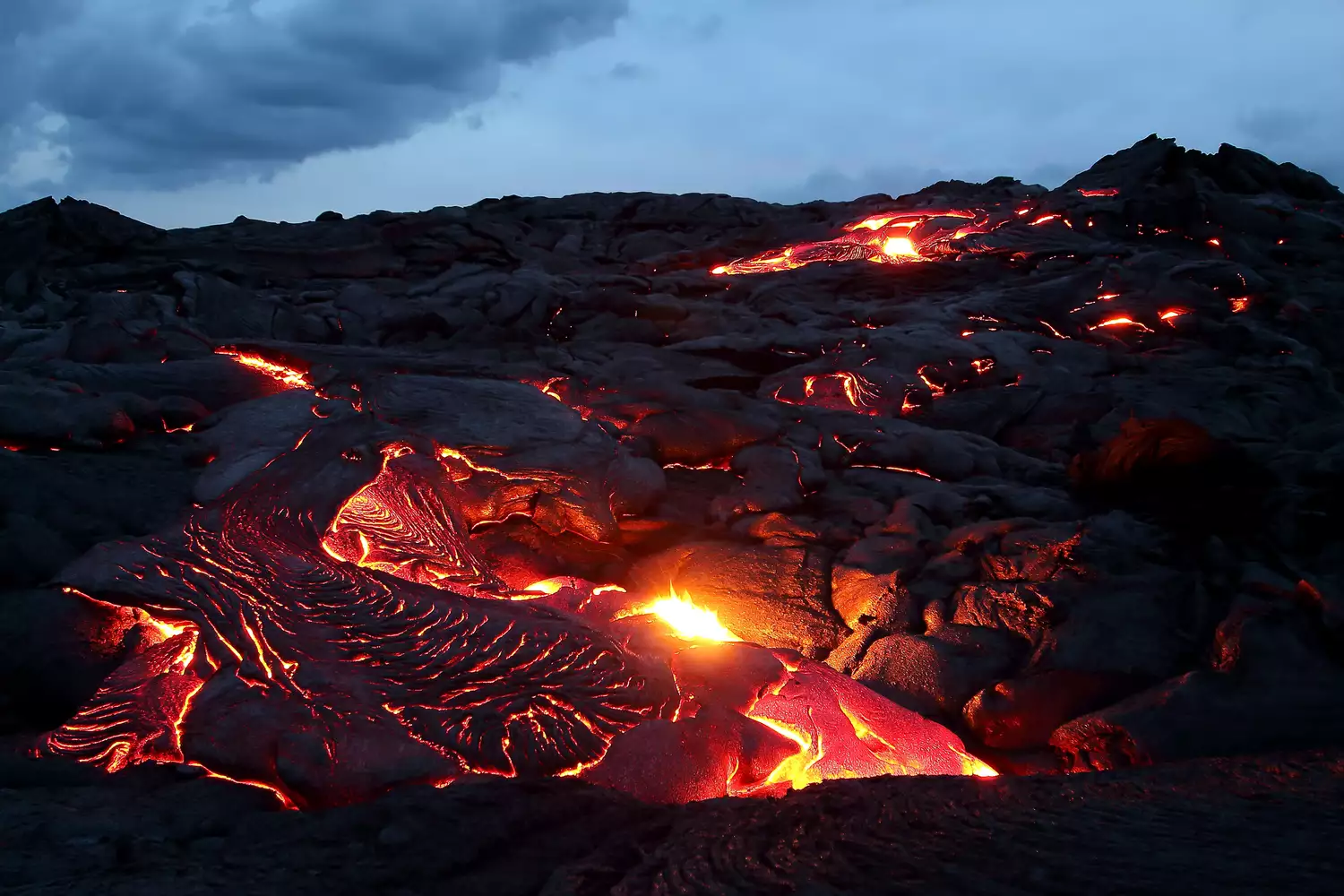 Светящийся оранжевый поток лавы над темными вулканическими породами
