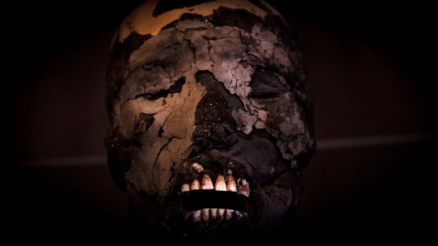 Лицо мумии Чинчорро с виднеющимися зубами на темном фоне